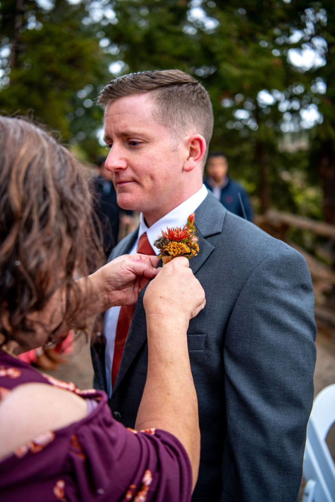 Mother of the groom pins boutonniere on her son before his wedding at Sapphire Point, CO.