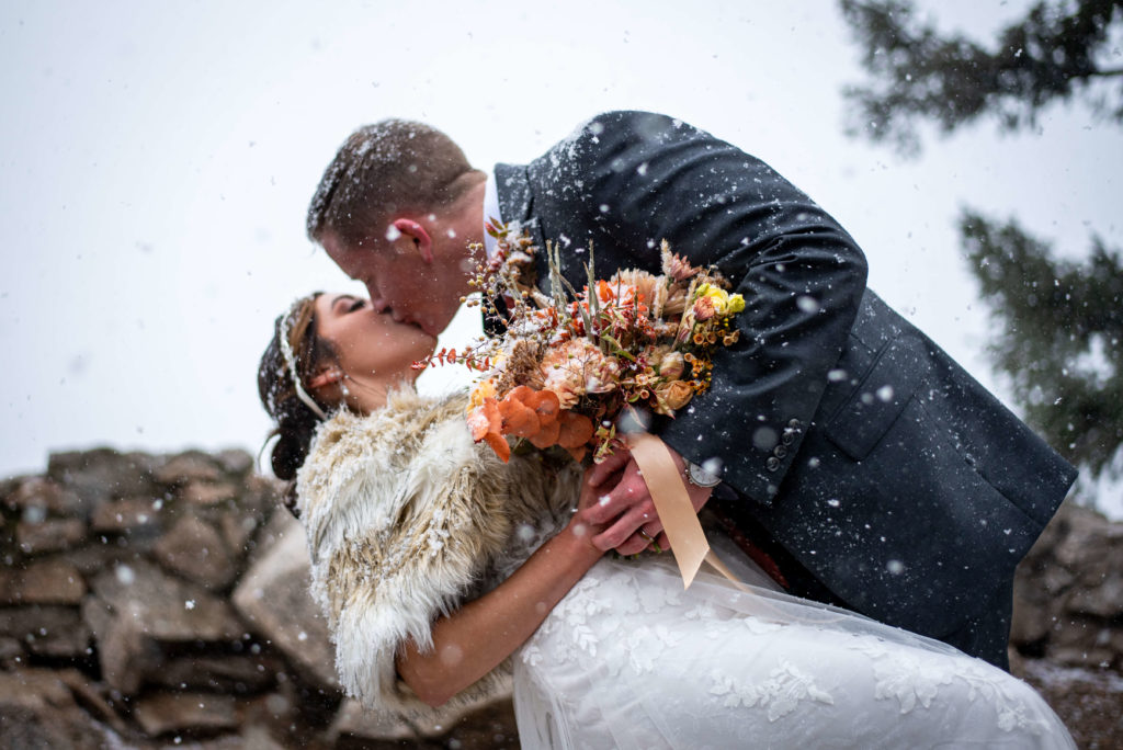 A man and woman share their first kiss in the snow after their intimate elopement ceremony. The groom dips his bride.