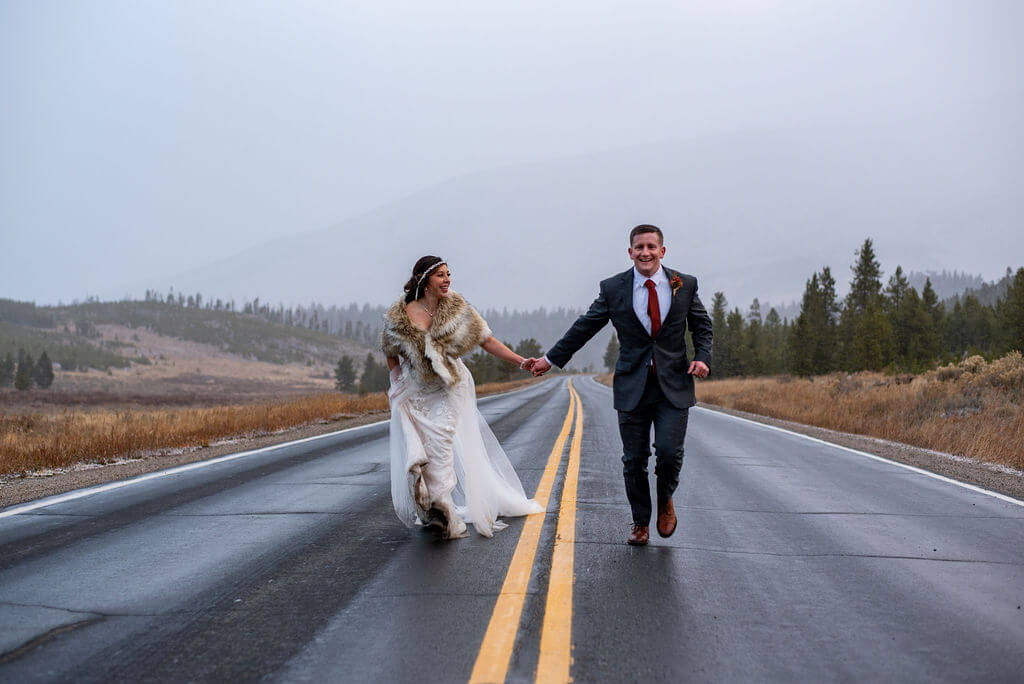 Bride and groom run up the road holding hands to celebrate their elopement.