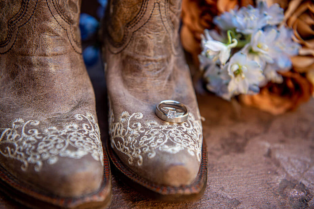 Wedding bands positioned on the brides cowboy boots with her bridal bouquet in the background. 
