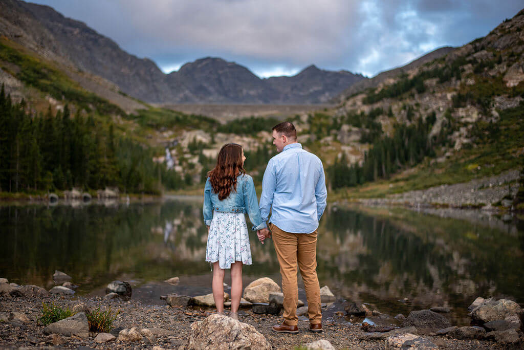 Couple face away from their Breckenridge Engagement photographer while looking out at a mountain lake. 