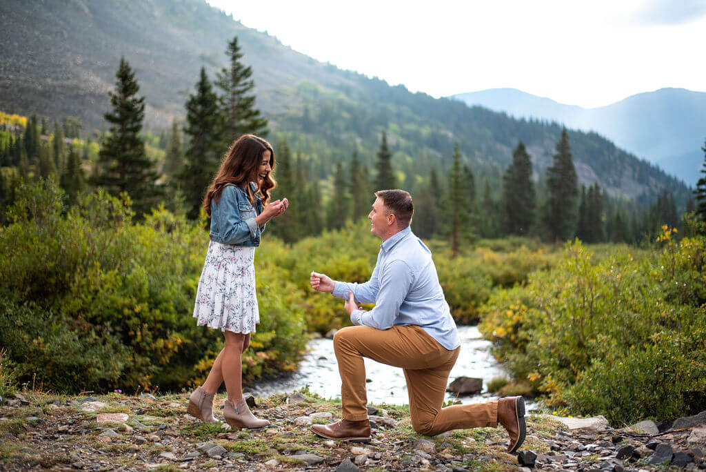 Man kneels down with a ring and proposes to a woman in front of their Breckenridge engagement photographer