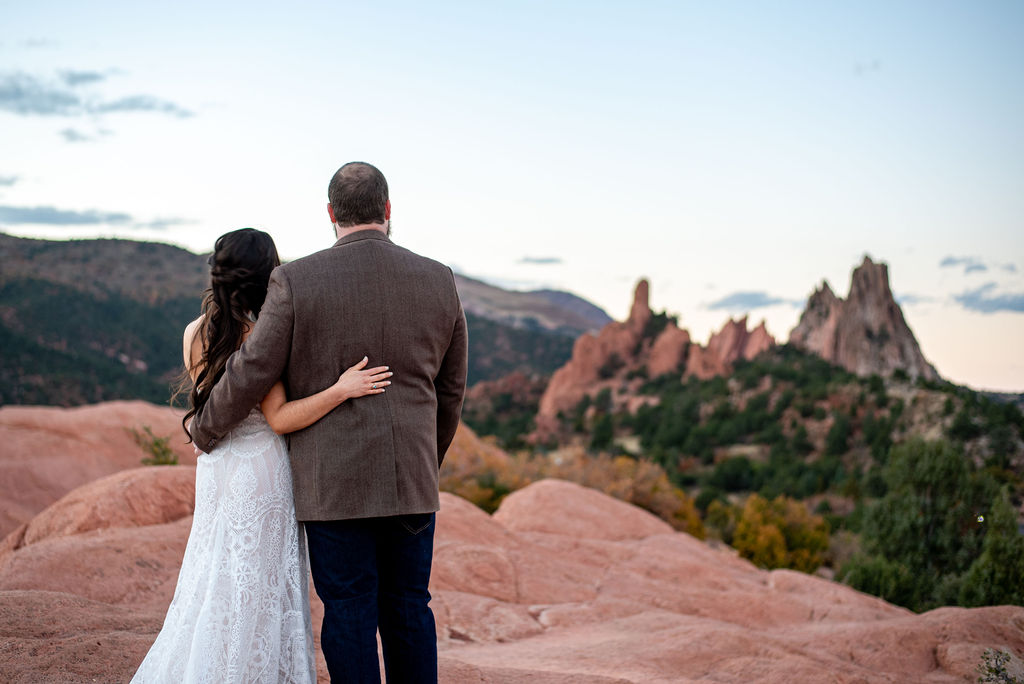 Bride and groom face a rock formation at Garden of the gods park with their arms around each other.