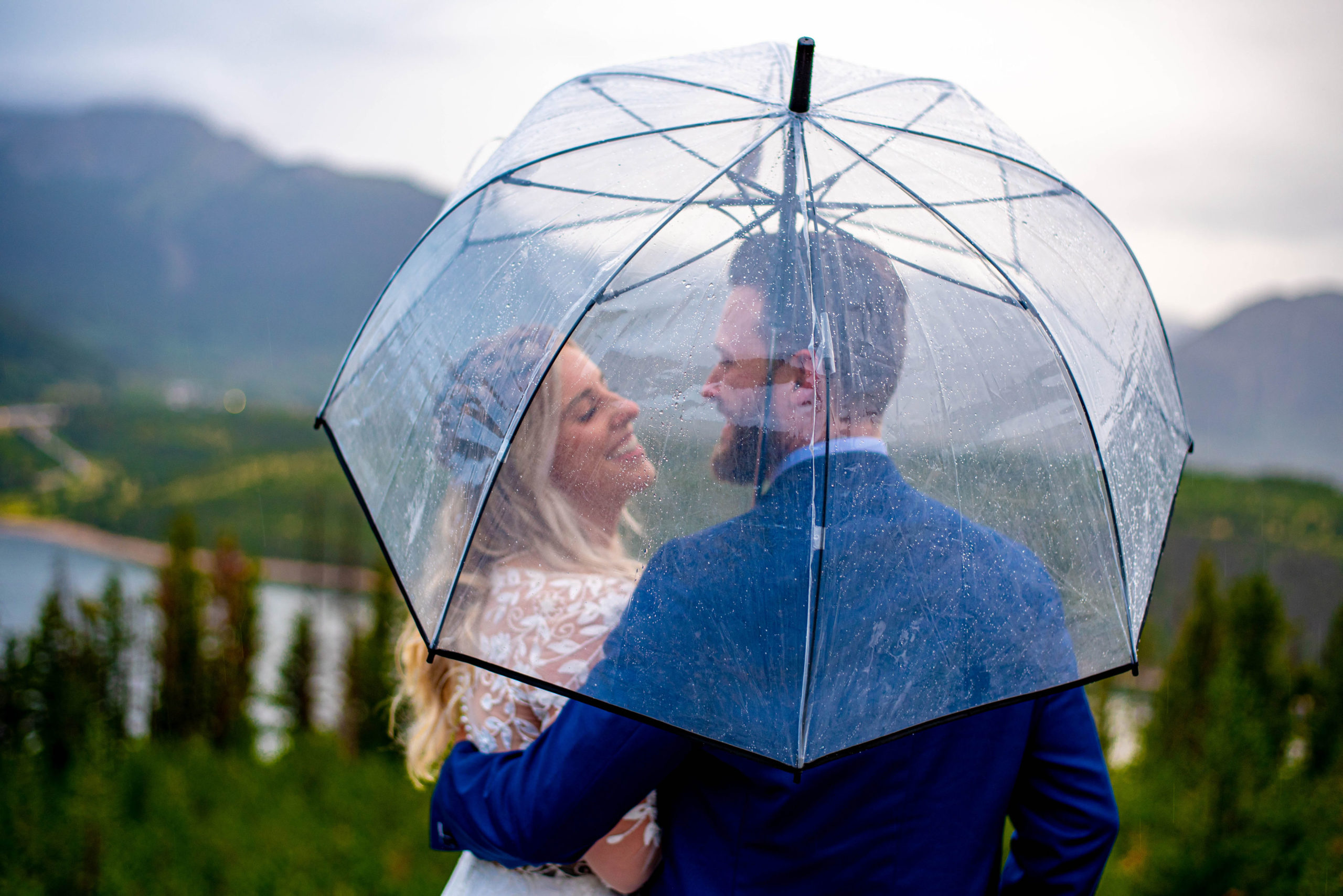 bride and groom smile to each other under an umbrella while it rains during their Colorado mountain elopement