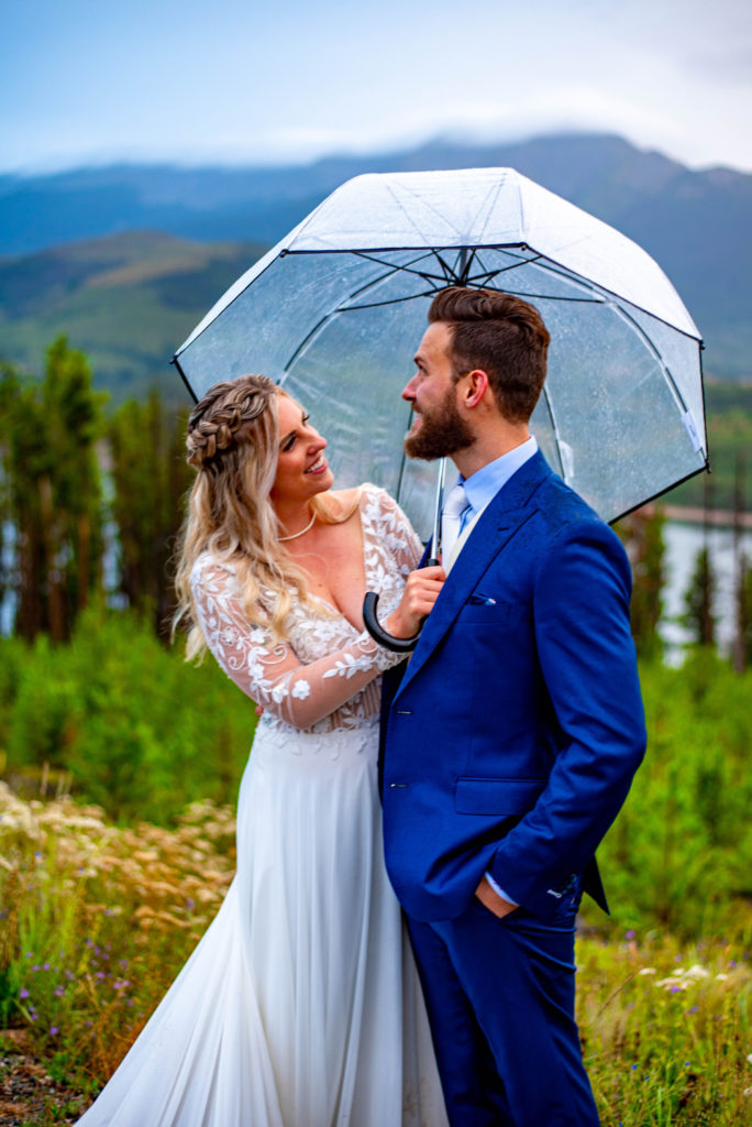 Bride and groom laugh under an umbrella while it rains following their Colorado mountain elopement