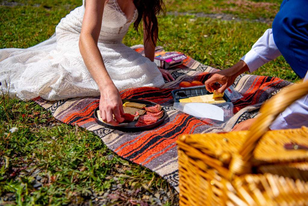 A bride and a groom sit on a blanket and eat snacks during their elopement in Crested Butte