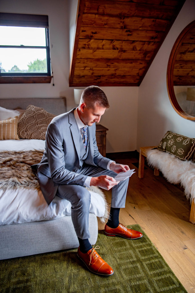 groom reads over his wedding vows on the edge of the bed
