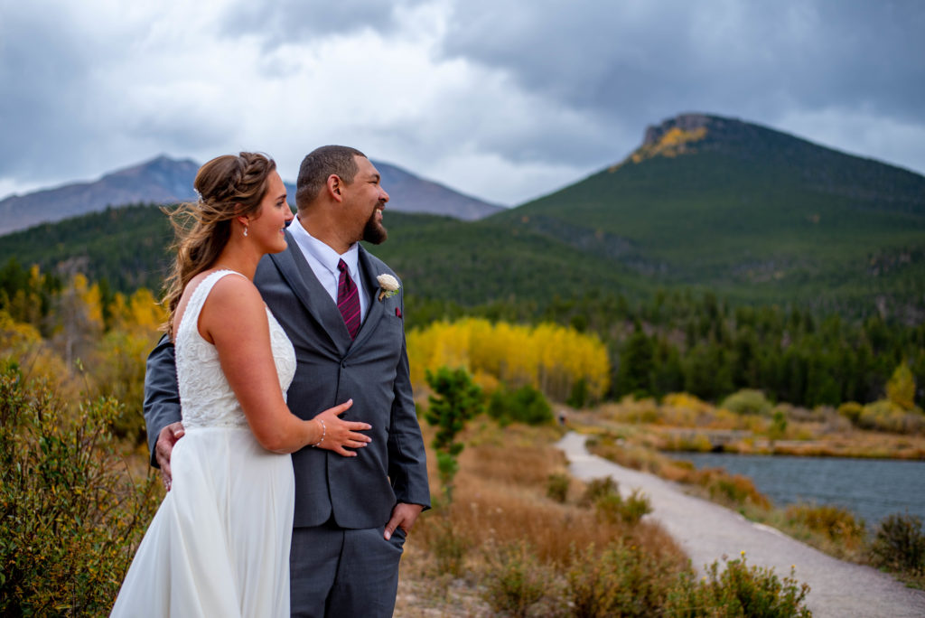 Bride and groom look out across an alpine lake in Rocky Mountain National Park in the fall.