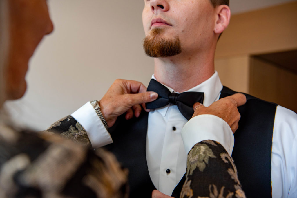 This is a close up image of a woman's hands as she helps to fix the grooms tie. 