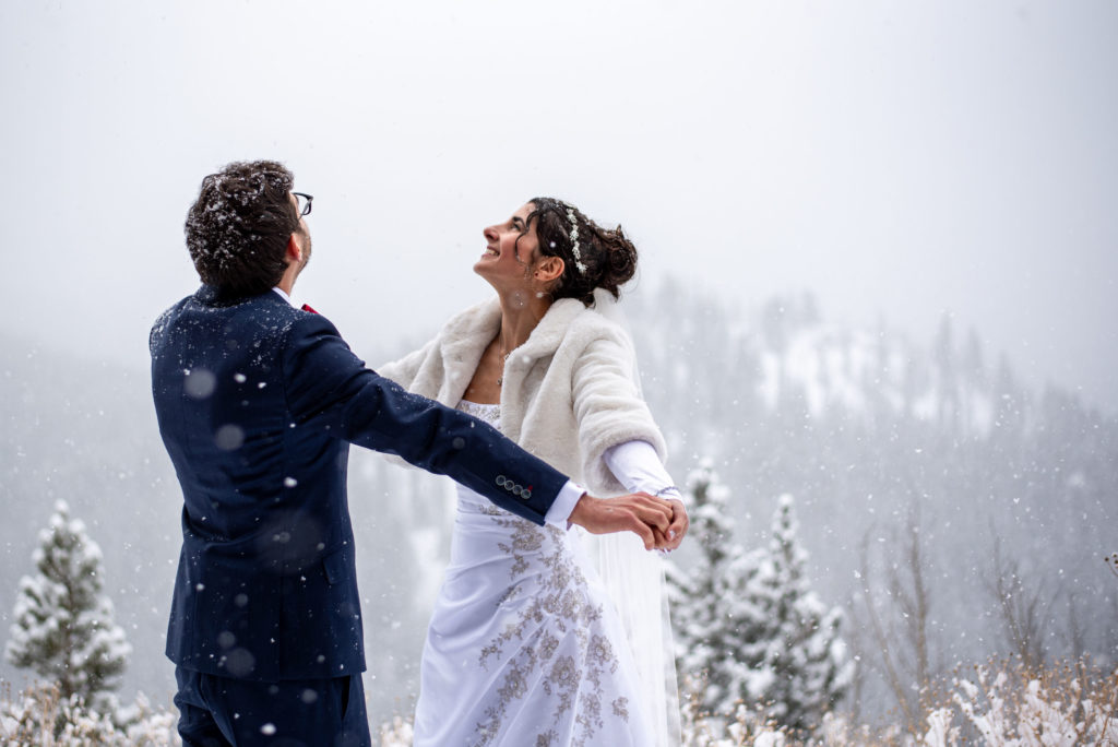 a bride and a groom hold hands as they look into the sky while in the middle of a snow storm