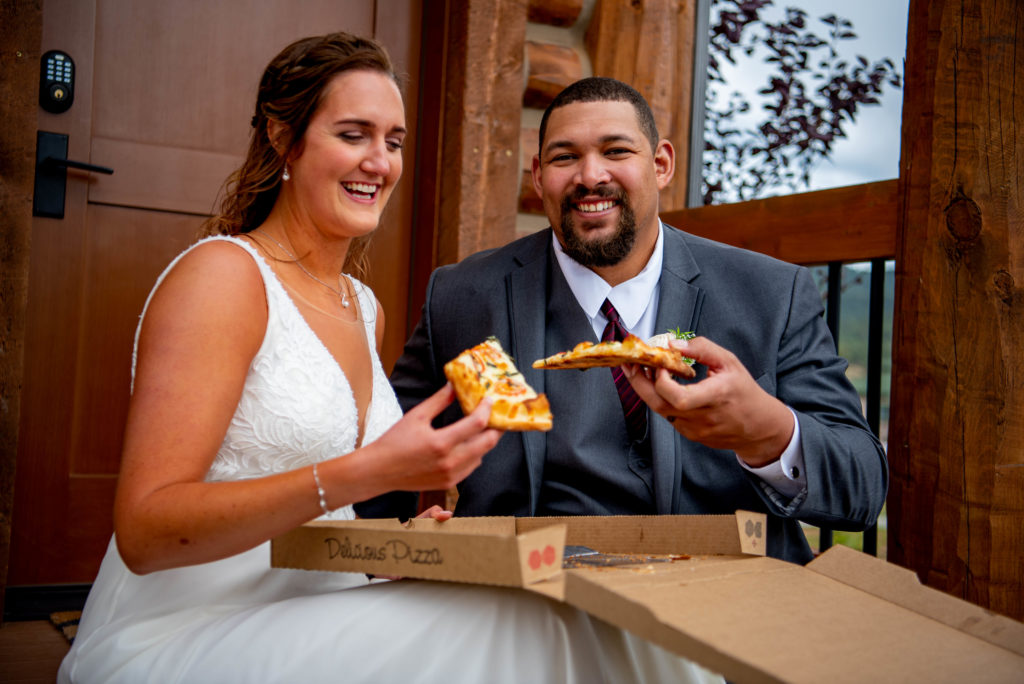 bride and groom share a slice of pizza at a reception including family in their elopement.