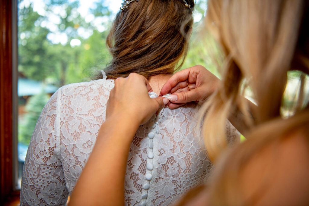 a picture of a woman's hands as she helps to button up a bride's wedding dress. 
