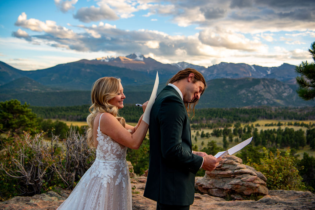 A bride is signing the marriage license on her husbands back after their rocky mountain national park elopement. They are standing profile with mountains in the background. 