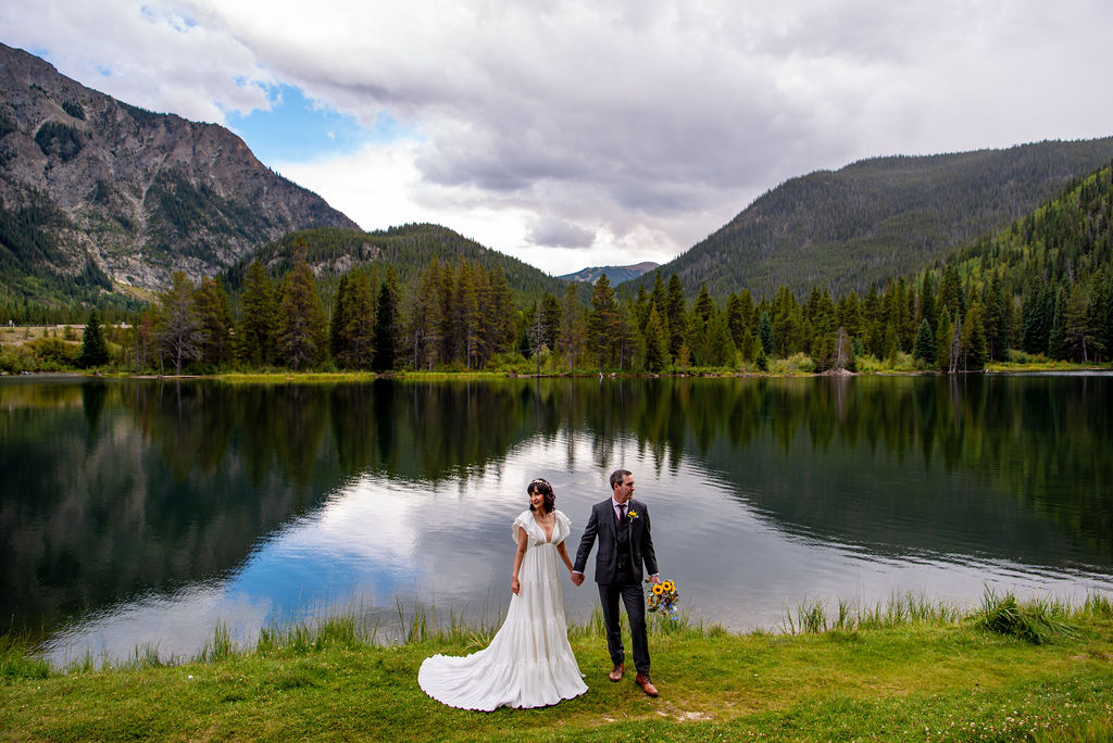 bride and groom walking hand in hand at a beautiful lake shore in Breckenridge, CO