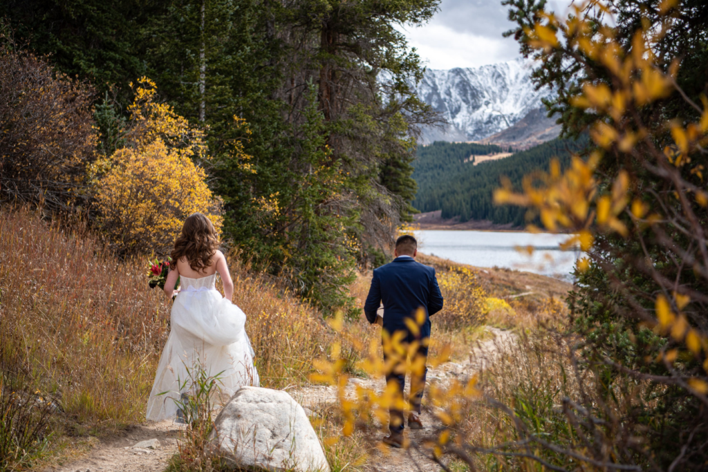 bride and groom walking on a trail together, surrounded by fall foliage in colorado