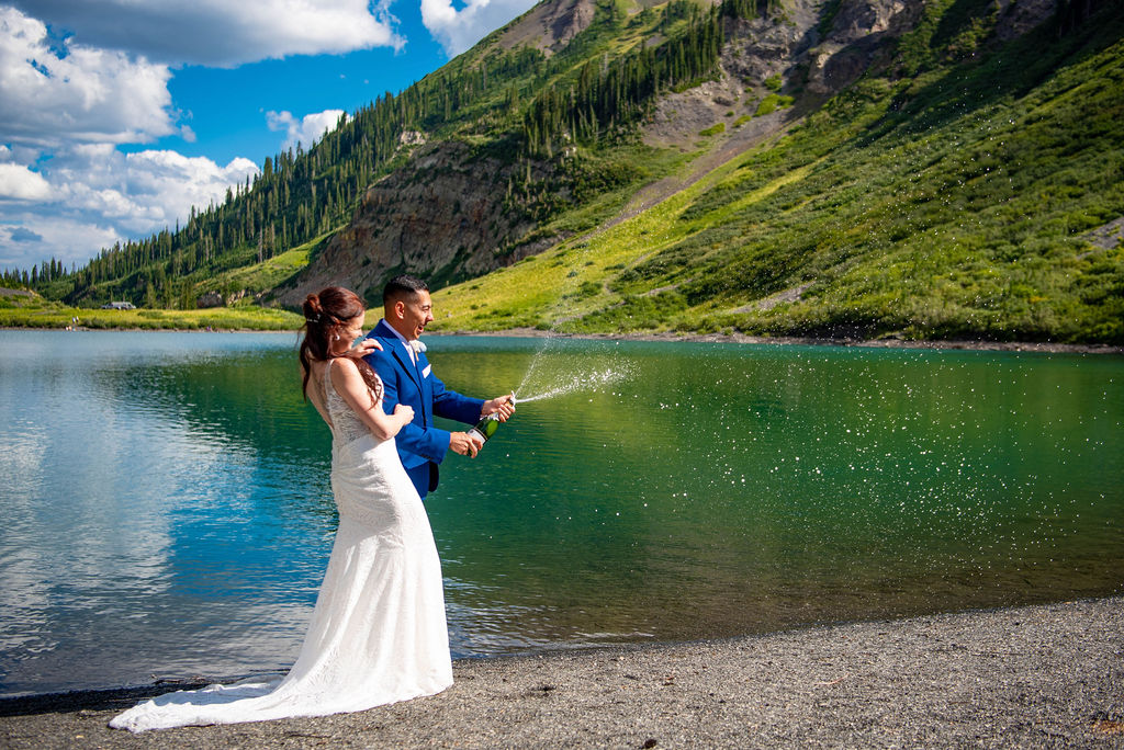 bride and groom popping champagne at a lake shore