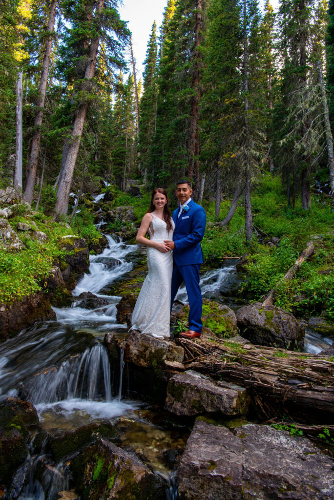 bride and groom posing together in a lush forest with a small waterfall in the backdrop