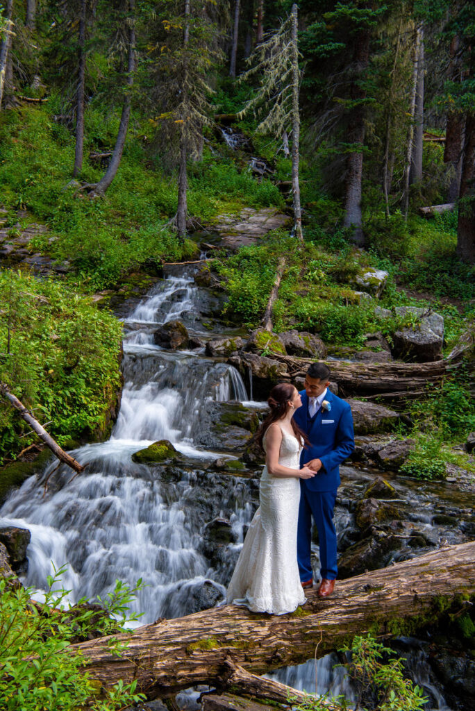 bride and groom posing together in a lush forest with a small waterfall in the backdrop