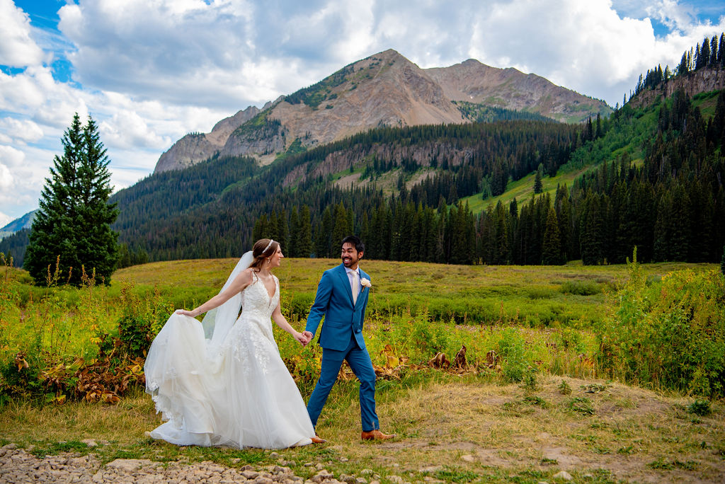 bride and groom running through a lush field holding hands with mountains in the backdrop for their Crested Butte elopement