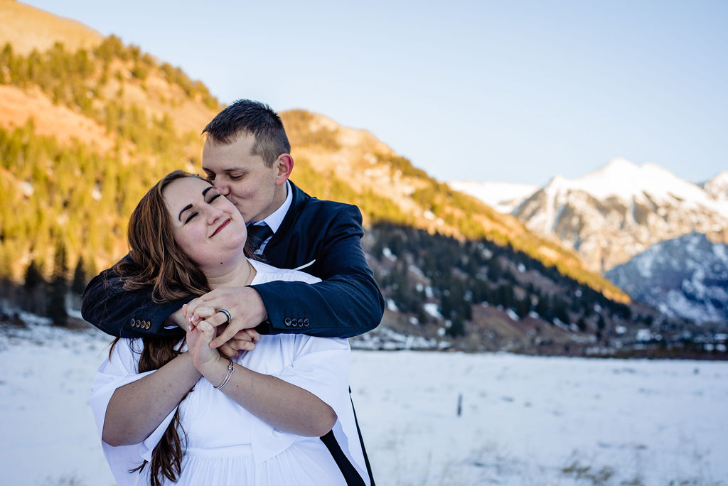 groom hugging his bride from behind with mountains in the backdrop