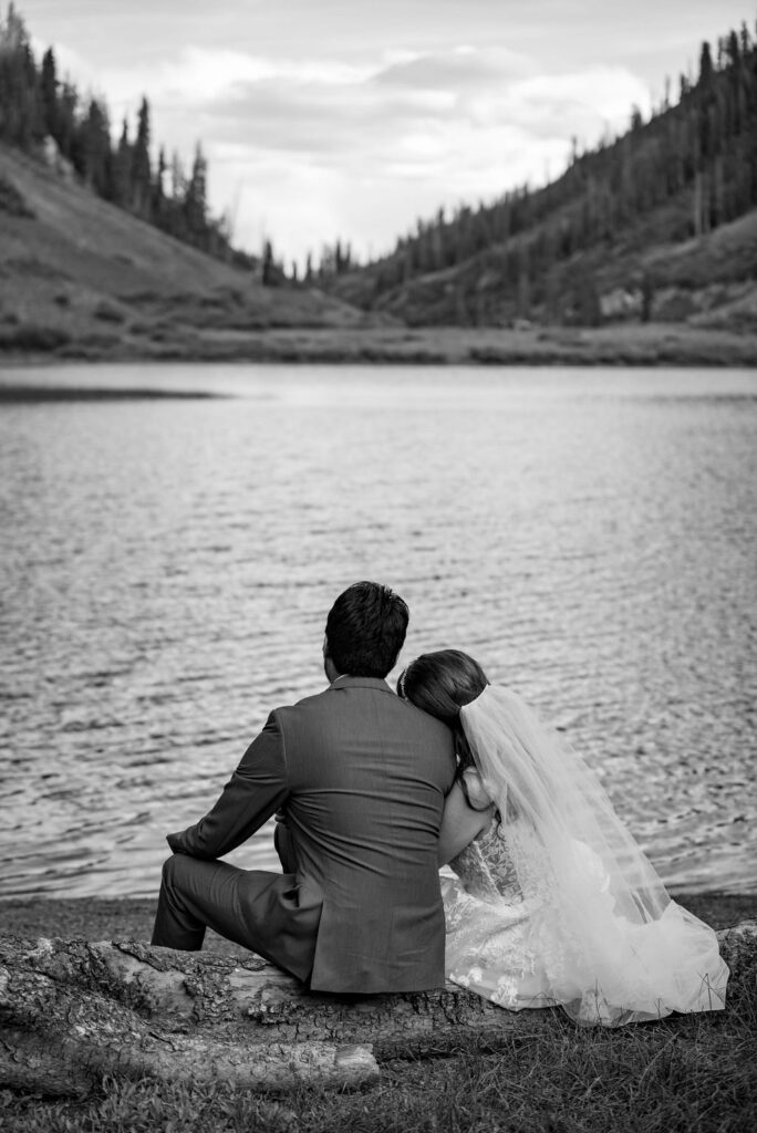 romantic bride and groom sitting down by an alpine lake