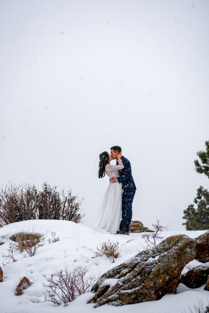 bride and groom kissing while snow is slowly falling around them