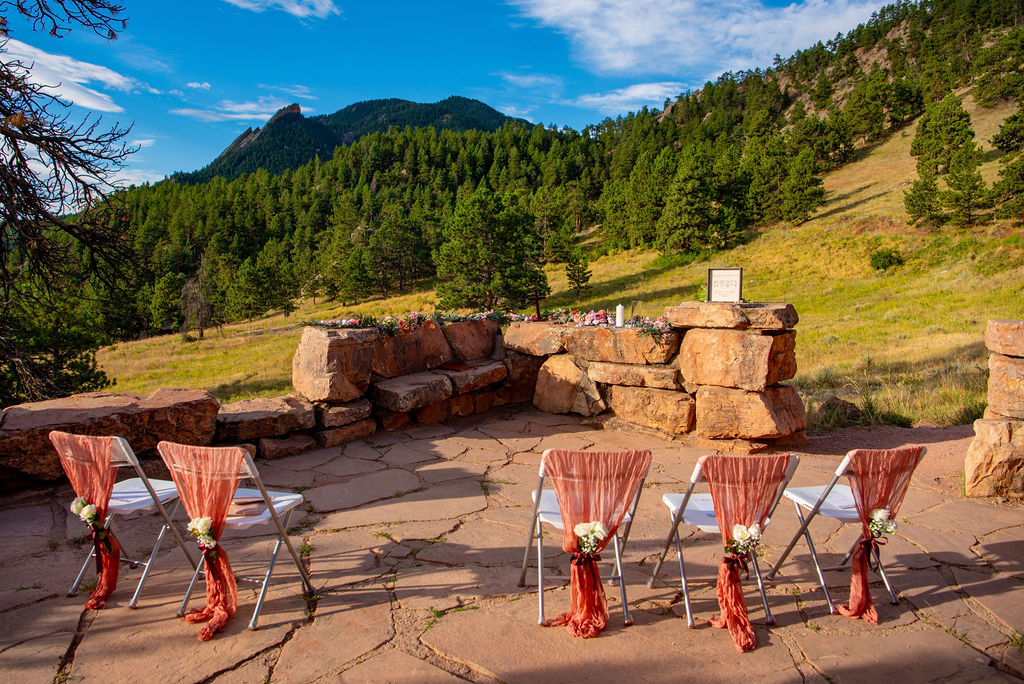 Intimate outdoor Boulder Halfway House wedding ceremony setup with decorated chairs and a mountain backdrop.