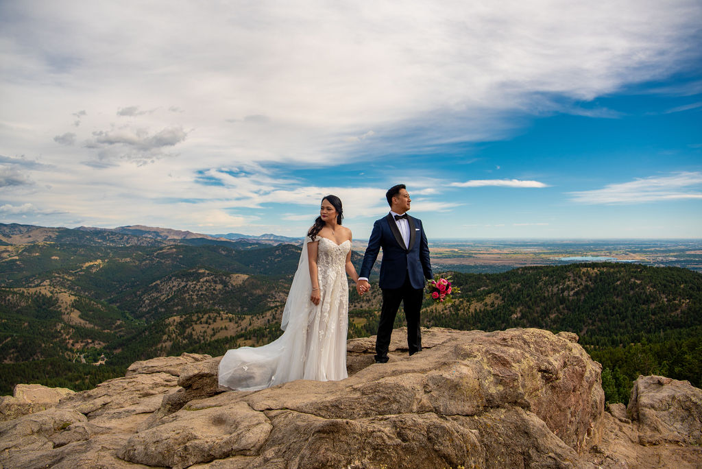 Bride and groom standing on a rocky mountaintop, hand in hand, overlooking vast mountain views and a dramatic sky near Boulder, Colorado. A powerful moment frozen by a Boulder Colorado elopement photographer.