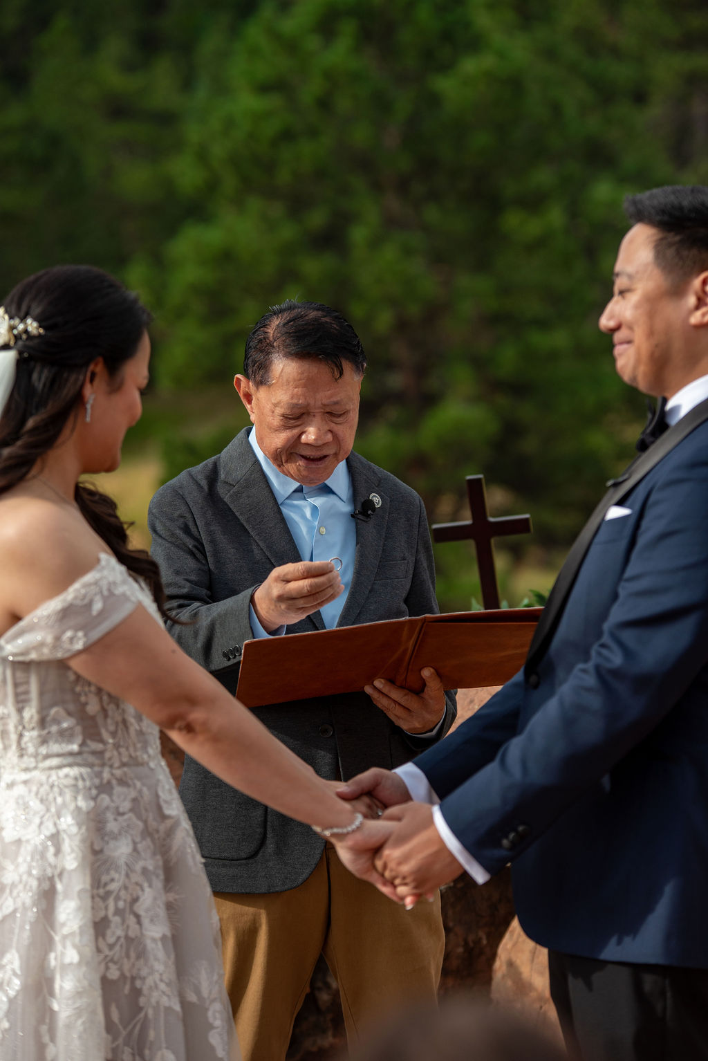 Officiant presenting wedding ring during a Boulder Halfway House wedding ceremony as the couple holds hands in a natural mountain setting."