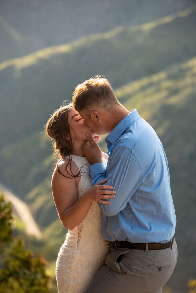 A couple shares a tender kiss outdoors, surrounded by a blurred mountainous backdrop. The moment is intimate, with warm, natural lighting. All their Colorado elopement planning was worth it.