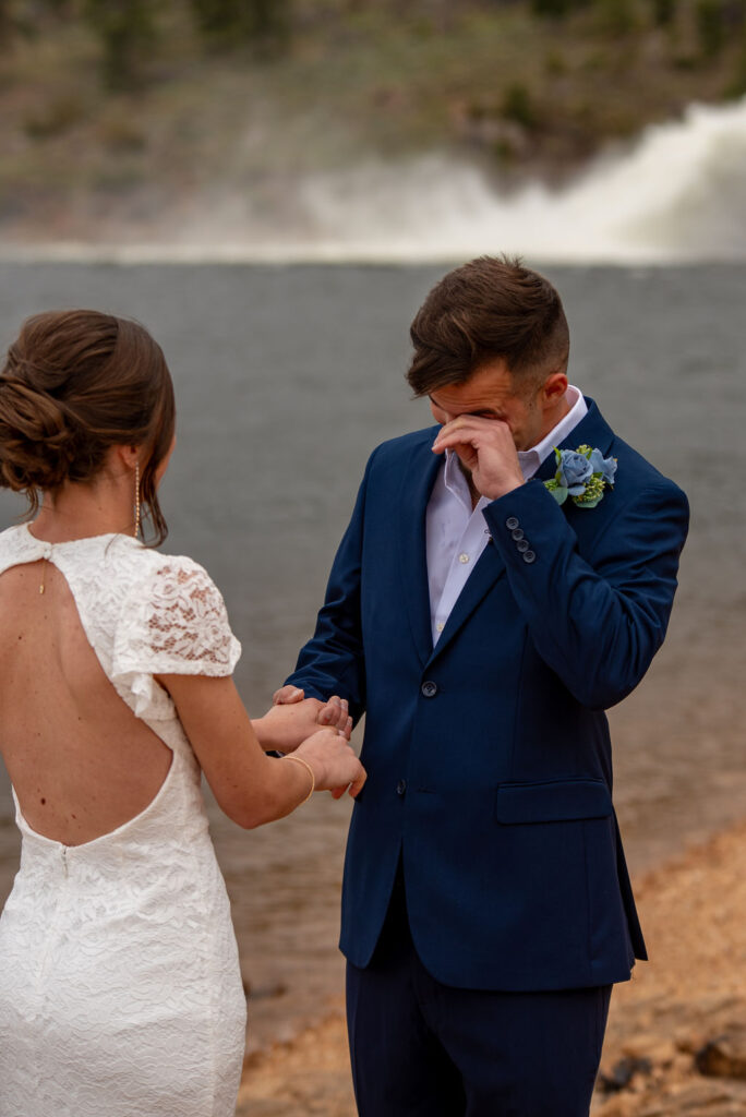 Groom wipes away tears while holding hands with his bride during their emotional elopement ceremony at Mary’s Lake. Captured by an Estes Park elopement photographer, this candid moment reflects the deep emotion of a private mountain wedding.