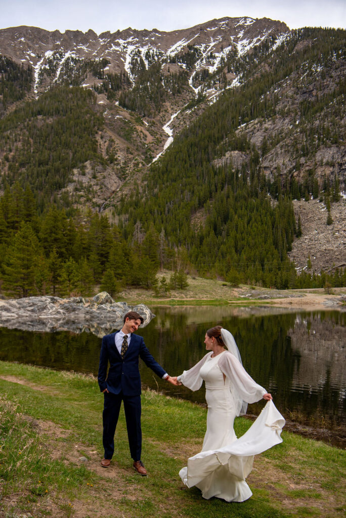 A romantic moment from a Colorado wedding captured by the Breckenridge wedding photographer, featuring a couple in elegant attire with towering mountains in the background. The bride is twirling her dress and the groom is admiring her.