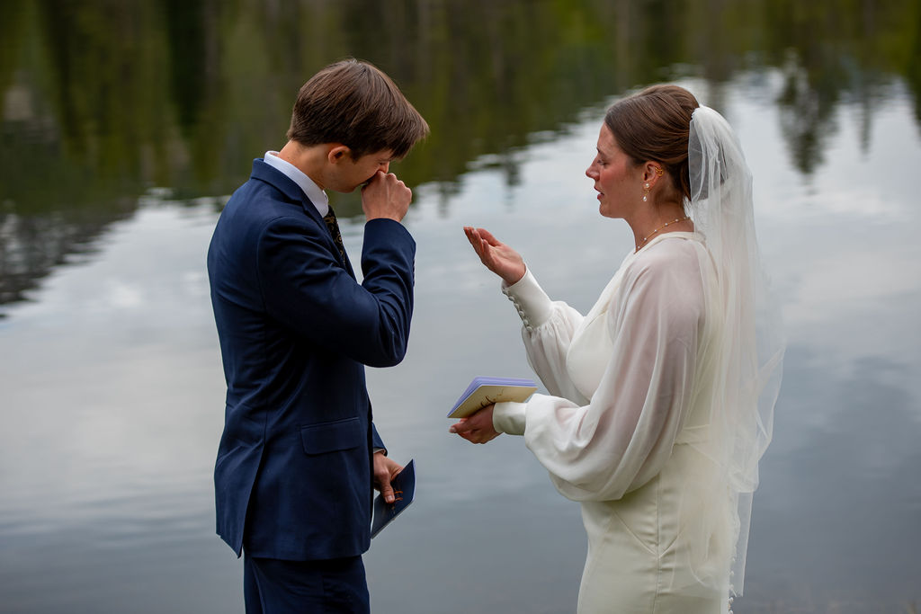 A man in a suit and a woman in a white wedding dress are standing facing each other in front of a lake. they are are both crying as they are saying their wedding vows. The Breckenridge wedding photographer captures the scene during their elopement ceremony.