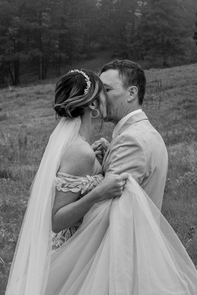 A bride and groom share a kiss in a scenic Colorado field, celebrating their love and the beauty of their wedding day. The Colorado Wedding photographer captures this candid moment perfectly.
